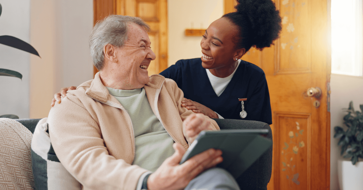 Senior man sitting next to caregiver laughing.