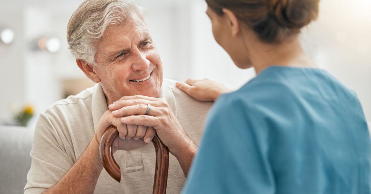 Caregiver comforting older man with cane in assisted living.